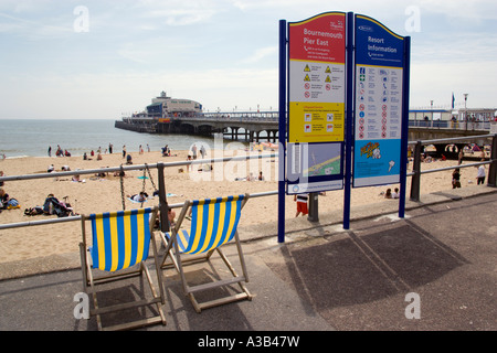 Inghilterra Bournemouth Dorset est turisti in spiaggia a prendere il sole sulla sabbia accanto a località balneare pier con informazioni segno e sdraio Foto Stock