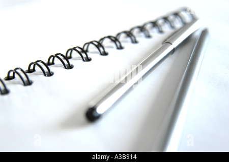 Libro bianco con rilegatura a spirale nera, penna in acciaio inox e matita in argento. Scatto con profondità di campo poco profonda. Foto Stock