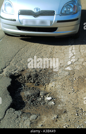 Grande pothole profondo non marcato al bordo della strada all'interno della linea bianca area guidabile con auto adiacente pot hole riparazione richiesto Essex Inghilterra UK Foto Stock