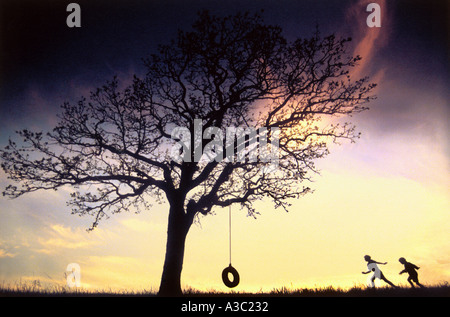 Silhouette di due bambini in esecuzione ad albero con tire swing tramonto Foto Stock