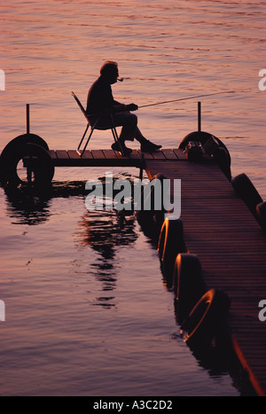 Silhouette di un uomo anziano di fumare un tubo e la pesca al largo un dock in Brainerd Minnesota Foto Stock