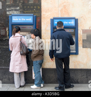 Torna & vista laterale di persone in piedi in e mediante la Barclays Bank ATM foro nella parete punto di contanti erogazione macchine denaro Londra Inghilterra REGNO UNITO Foto Stock
