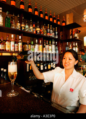 Oriental donna asiatica dietro un bar indossando bianco uniforme giacca, versando un bicchiere di Champagne Foto Stock