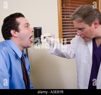 Medico utilizza un abbassa lingua per esaminare l'interno della sua bocca del paziente. Foto Stock