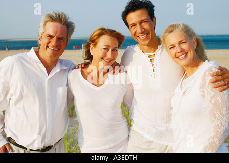 Ritratto di due coppie mature in piedi con le braccia intorno a ogni altro sulla spiaggia Foto Stock