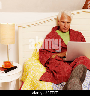 Uomo maturo di seduta sul letto e utilizzando un computer portatile Foto Stock