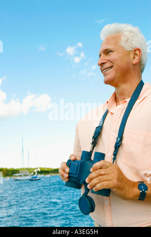 Uomo maturo tenendo un paio di binocoli e sorridente Foto Stock