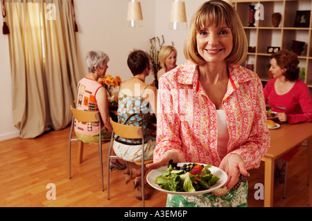 Ritratto di una donna matura tenendo un piatto di insalata e i suoi amici seduti dietro di lei Foto Stock