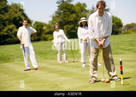 Ritratto di una metà uomo adulto giocando croquet con una coppia matura e metà donna adulta dietro di lui Foto Stock