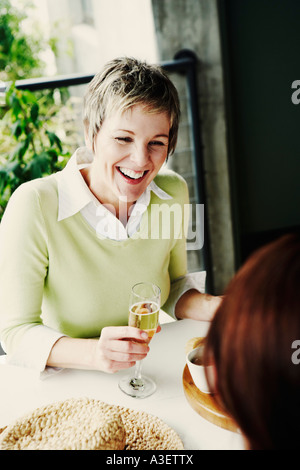 Donna matura tenendo un flute da champagne e sorridente con i suoi amici Foto Stock