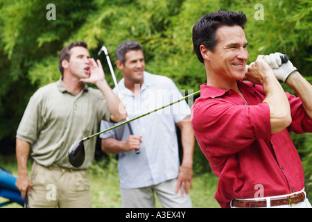 Uomo maturo oscillazione un golf club con i suoi amici in piedi dietro di lui Foto Stock