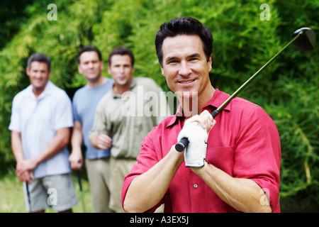 Uomo maturo tenendo un golf club con i suoi amici in piedi dietro di lui Foto Stock