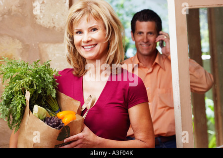 Ritratto di una donna matura tenendo un sacchetto della spesa con un uomo maturo a parlare su un telefono mobile dietro di lui Foto Stock