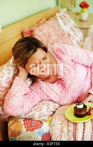 Angolo di alta vista di una donna matura giacente sul letto e tenendo una piastra di torta Foto Stock