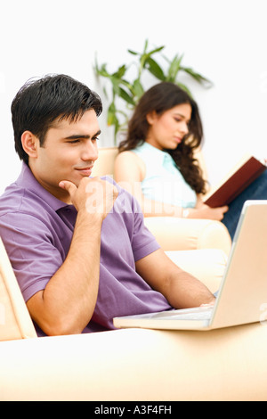 Profilo laterale di un giovane uomo che guarda un notebook con una giovane donna seduta in background Foto Stock