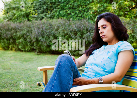 Metà donna adulta seduto in poltrona in un prato e utilizzando un telefono cellulare Foto Stock