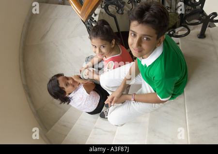 Angolo di alta vista di tre bambini seduti su una scalinata e sorridente Foto Stock