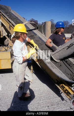 Maschi e femmine di lavoratori edili colata di calcestruzzo bagnato su nuovo Interstate Highway barriera mentre i lavoratori di sesso maschile esaminare barriera Foto Stock