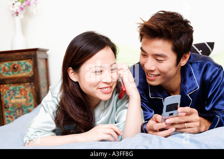 Close-up di una giovane donna che parla al cellulare con una metà uomo adulto che giace accanto a lei Foto Stock