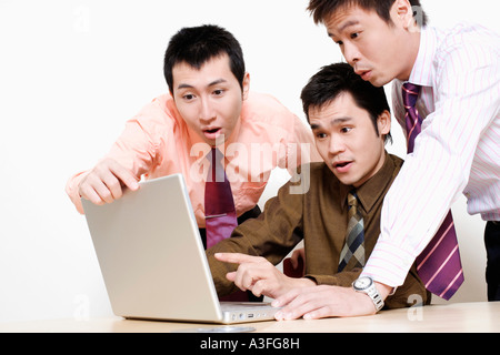 Tre uomini di affari con un computer portatile e guardando sorpresa Foto Stock