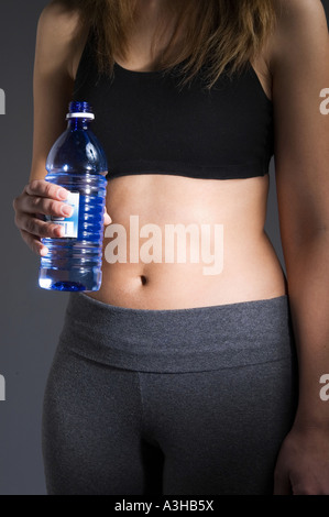 Fotografia di una donna di metà sezione indossando un nero reggiseno sportivo e grigio pantaloni di sudore e tenendo un blu bottiglia d'acqua. Foto Stock