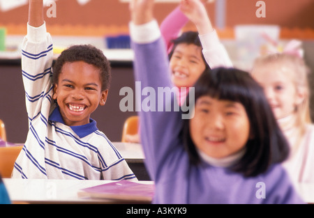 Gli studenti alzando le mani nella scuola elementare classroom Foto Stock