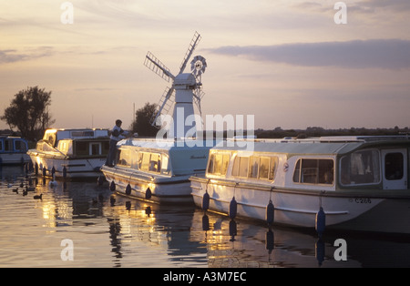 Thurne Staithe ormeggiati Vacanze barca di crociera con sun glint su windows di pompa di vento al di là di crepuscolo Foto Stock