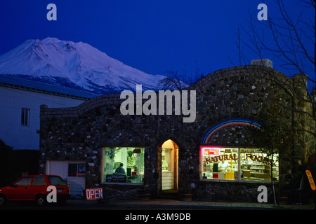 Coperta di neve per montaggio su telai Shasta grandi dietro la costruzione di pietra naturale di alloggiamento il negozio di alimentari e il cafe al crepuscolo in piccoli Califo settentrionale Foto Stock