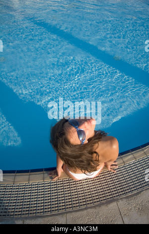 Giovane donna in bikini bianco seduto sul bordo della piscina, Italia Foto Stock