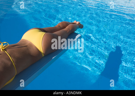 Giovane donna giacente sul trampolino sopra la piscina, Puglia, Italia Foto Stock