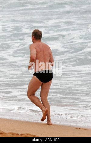 Un uomo di mezza età jogging o in esecuzione su una spiaggia in riva al mare Foto Stock