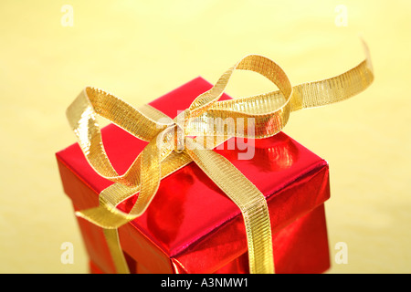 Red Regalo di natale con la prua in oro su sfondo dorato Foto Stock