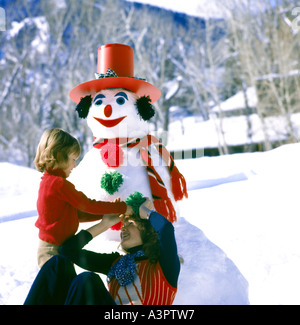 Giovane madre e suo figlio dare il tocco finale su un holly pupazzo di neve hanno costruito nel loro cortile anteriore su una giornata invernale Foto Stock