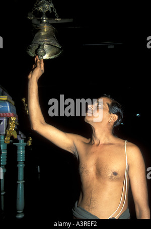 Un giovane prete di Brahmin suona la campana del tempio per la puja in un tempio indù Foto Stock