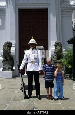 Due bambini europei stare accanto a un immobile guardie armate in uniforme al di fuori di un ingresso al Grand Palace, Bangkok, Thailandia Foto Stock