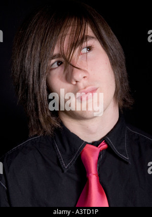 Giovane uomo di 16 anni in camicia nera e cravatta rosa guardando fiduciosi e riluttanti Foto Stock