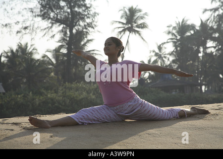 Donna seduta facendo yogic esercizi di stretching sulla spiaggia godendosi sole mare di sabbia Foto Stock