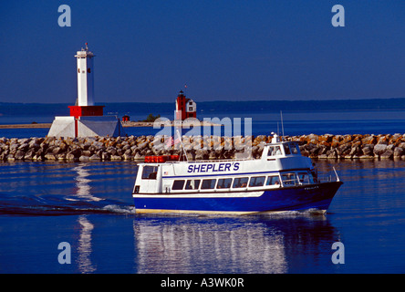 Un SHEPLER S FERRY BOAT ENTRA NELLA MACKINAC Island Harbour con una luce di frangiflutti e il Round Island Lighthouse IN BACKGROUND Foto Stock