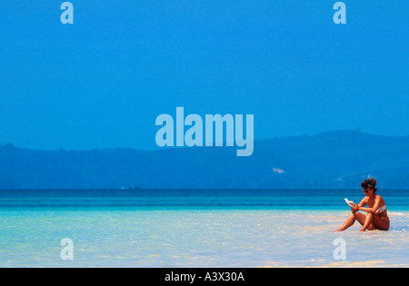 Bikini donna legge libro seduti sulla spiaggia in acque poco profonde della Thailandia Foto Stock