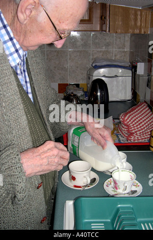 Maschio Senior facendo una tazza di tè aggiungendo il latte nella tazza prima che il latte. Foto Stock