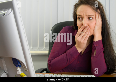 Scioccato giovane donna segretario o lavoratore di ufficio al banco guardando lo schermo del computer Foto Stock