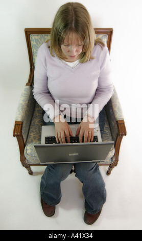 Giovane donna si siede su una poltrona tradizionale e i tipi sul suo computer portatile Foto Stock