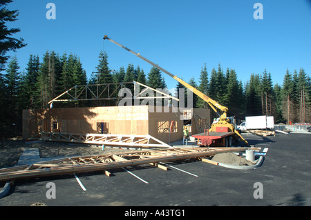 Costruzione - Ampia vista della gru mettendo in legno travatura del tetto in posizione con un altro travatura in primo piano nel parcheggio Foto Stock