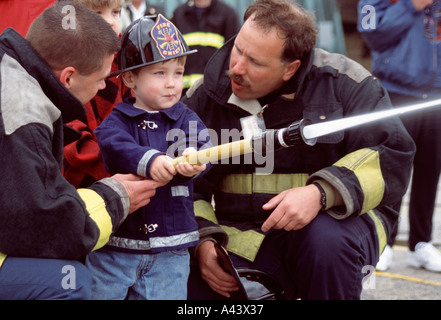 Due vigili del fuoco aiutare un giovane bambino con tubo flessibile di mettere fuori fuoco di dimostrazione nel midwest degli Stati Uniti Foto Stock