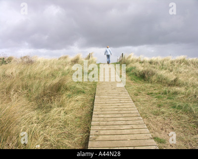 Ragazza sul tavolato in legno percorso attraverso marram grass duna di sabbia Foto Stock