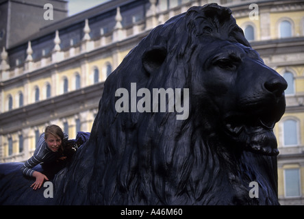 Un bambino si arrampica su di una scultura di Lion in corrispondenza della base della colonna di Nelson a Trafalgar Square a Londra Foto Stock