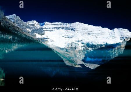 Innevate montagne rocciose riflessa sulle calme acque del Lago Louise, Canadian Rockies riflesso sul lago ancora Foto Stock