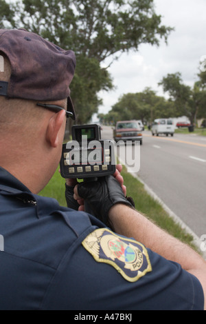 Motociclo funzionario di polizia utilizzando una pistola laser per misurare la velocità in un quartiere residenziale Foto Stock