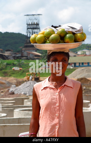 Villaggio locale donna trader, vassoio di trasporto delle arance sulla sua testa, sulla miniera d'oro sito in costruzione, Ghana, Africa occidentale Foto Stock