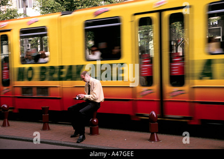 Amsterdam tram viaggiano a velocità passa dietro un passeggero con un telefono cellulare per inviare un messaggio di testo Foto Stock